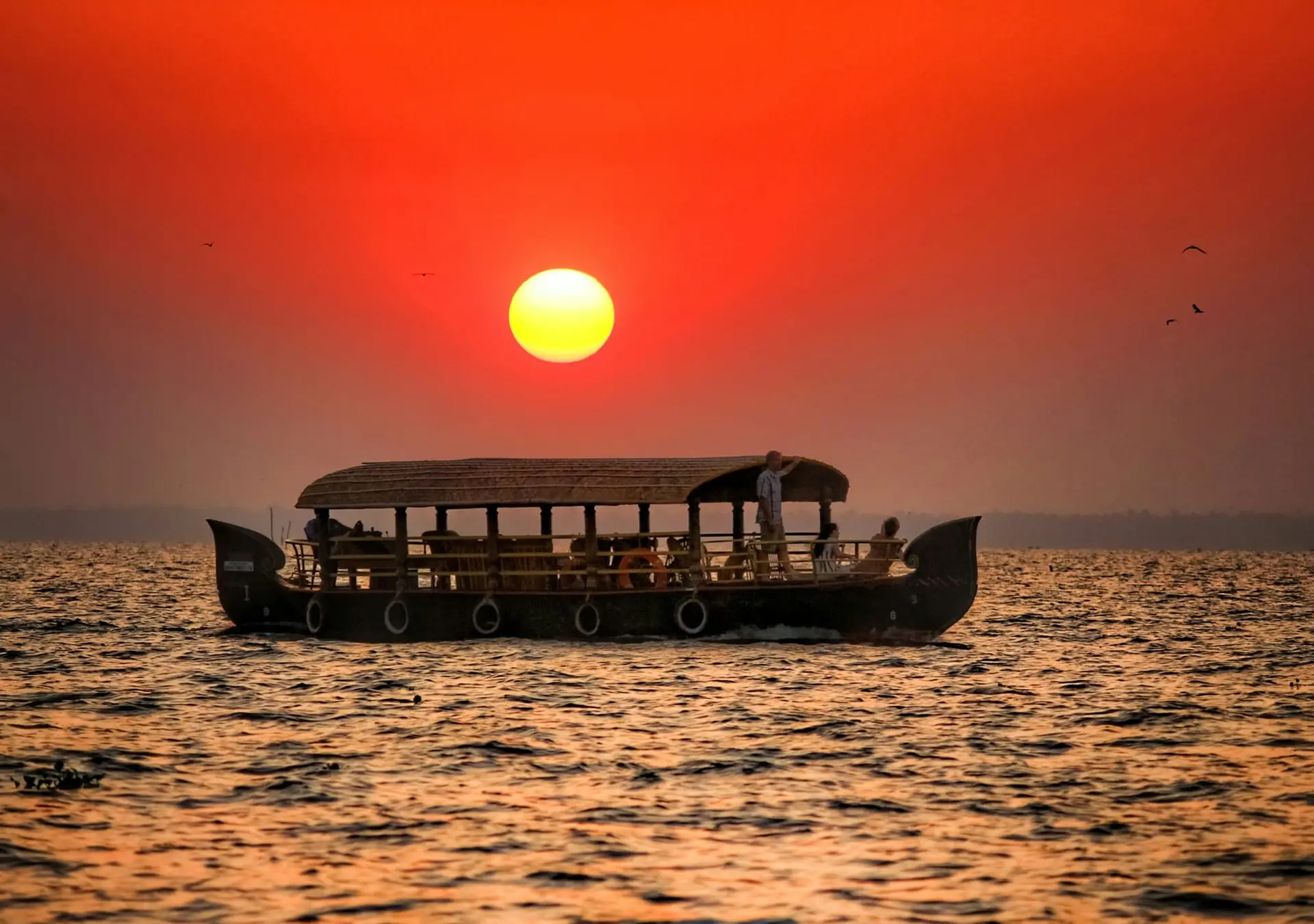 A houseboat silhouetted against a red sunset over the backwaters at Kumarakom