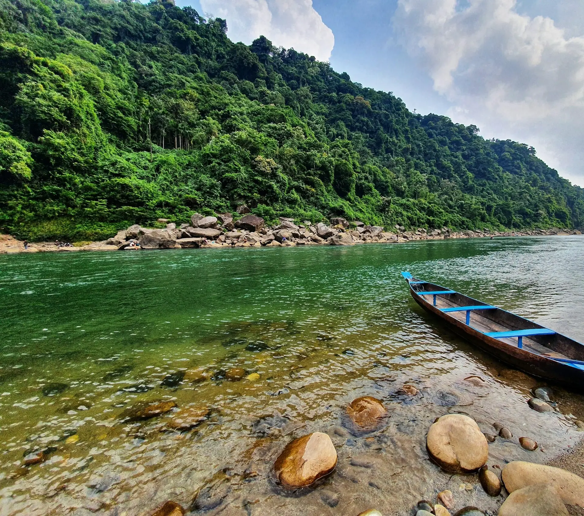 A long wooden boat resting at the edge of the green Umngot River