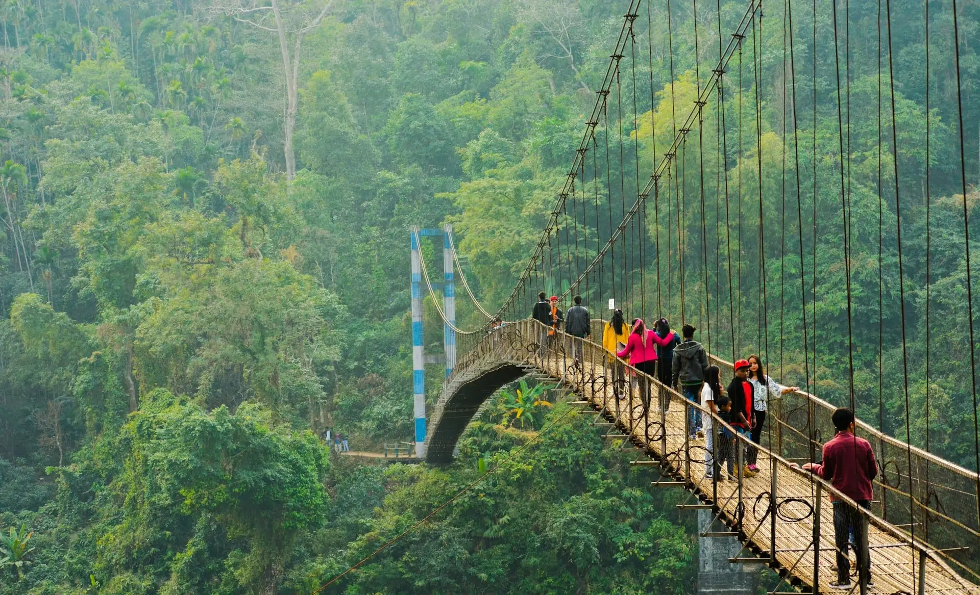 People crossing a suspension bridge over the river at Shnongpdeng