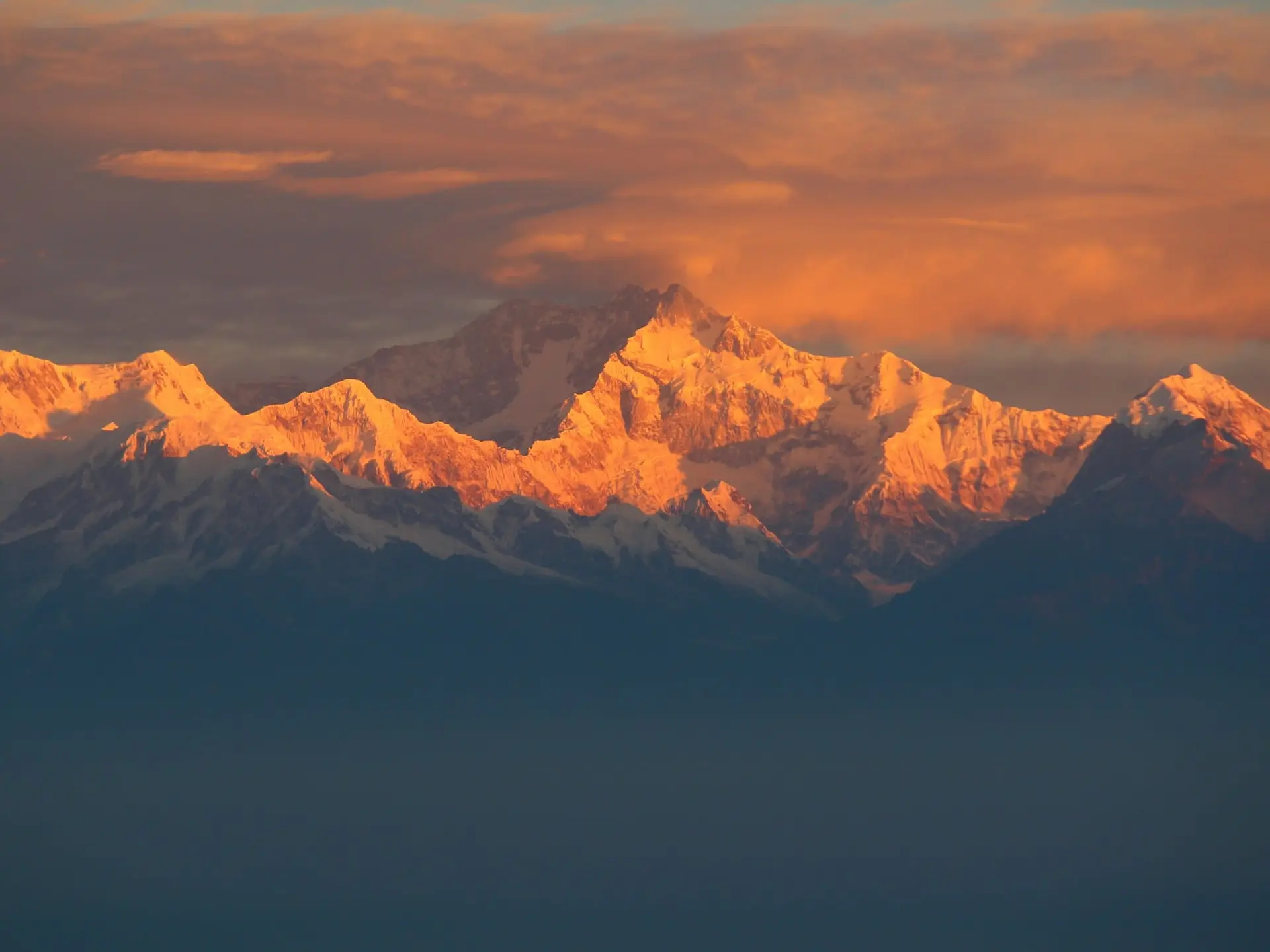 The summit of Kanchenjunga glowing gold at first light above dark Himalayan foothills